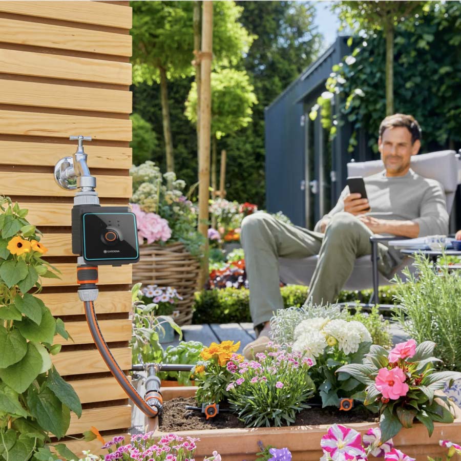 Smarte Bewässerungssteuerung von GARDENA und Mann mit Smartphone im Garten