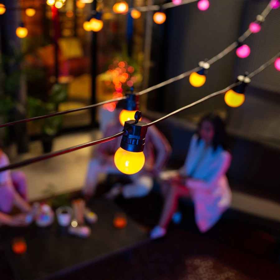 Smarte Lichterkette mit orangefarbenen Licht über Terrassentisch im Garten