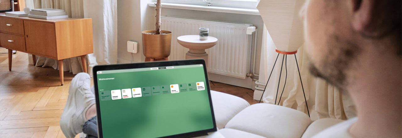Ein Mann schaut auf Darstellung von Steuerung des Smart Homes über Desktop App. Im Hintergund ist ein smartes Heizset am Heizkörper angebracht.
